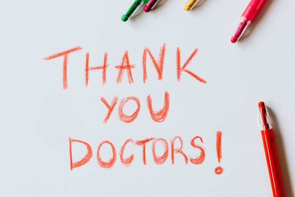 A handwritten 'Thank You Doctors!' note surrounded by colorful pens on a white surface.