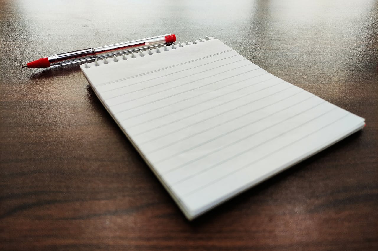 A lined notebook with a red pen on a wooden desk, perfect for school or office use.
